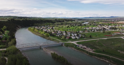 Image of the Bow River in Cochrane, Alberta looking west with a bridge and neighbourhood homes included.